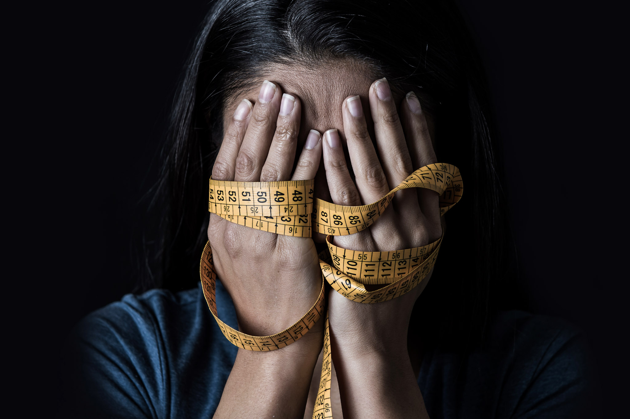 stock image of a woman's hands covering her face while also wrapped in measuring tape