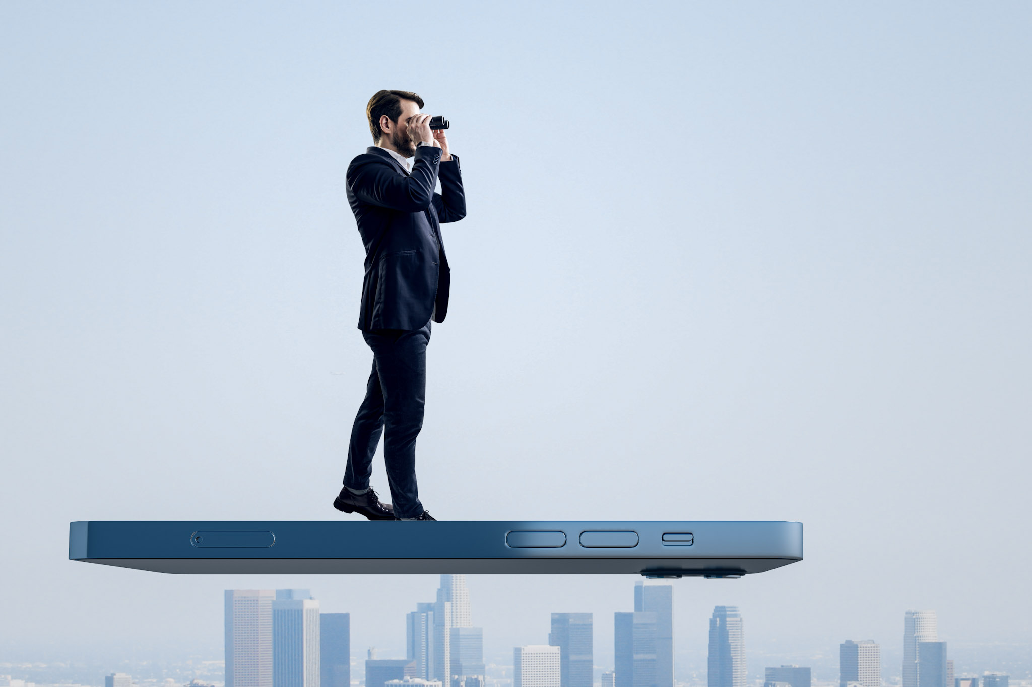 composite stock image of a man standing on a giant floating smartphone peering through binoculars, with a cityscape in the background distance