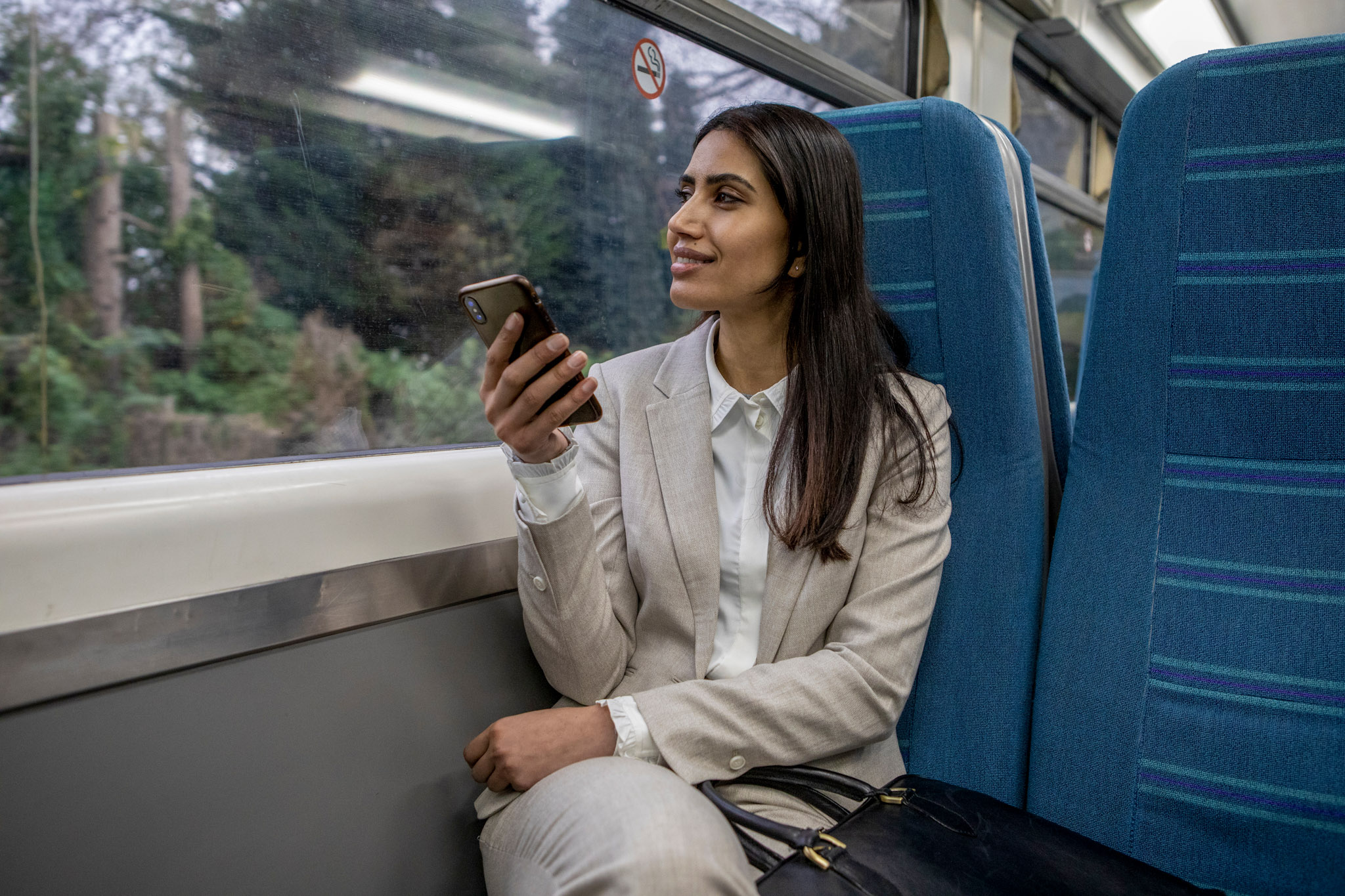 stock image of a business woman using a smartphone while seated inside a train carriage