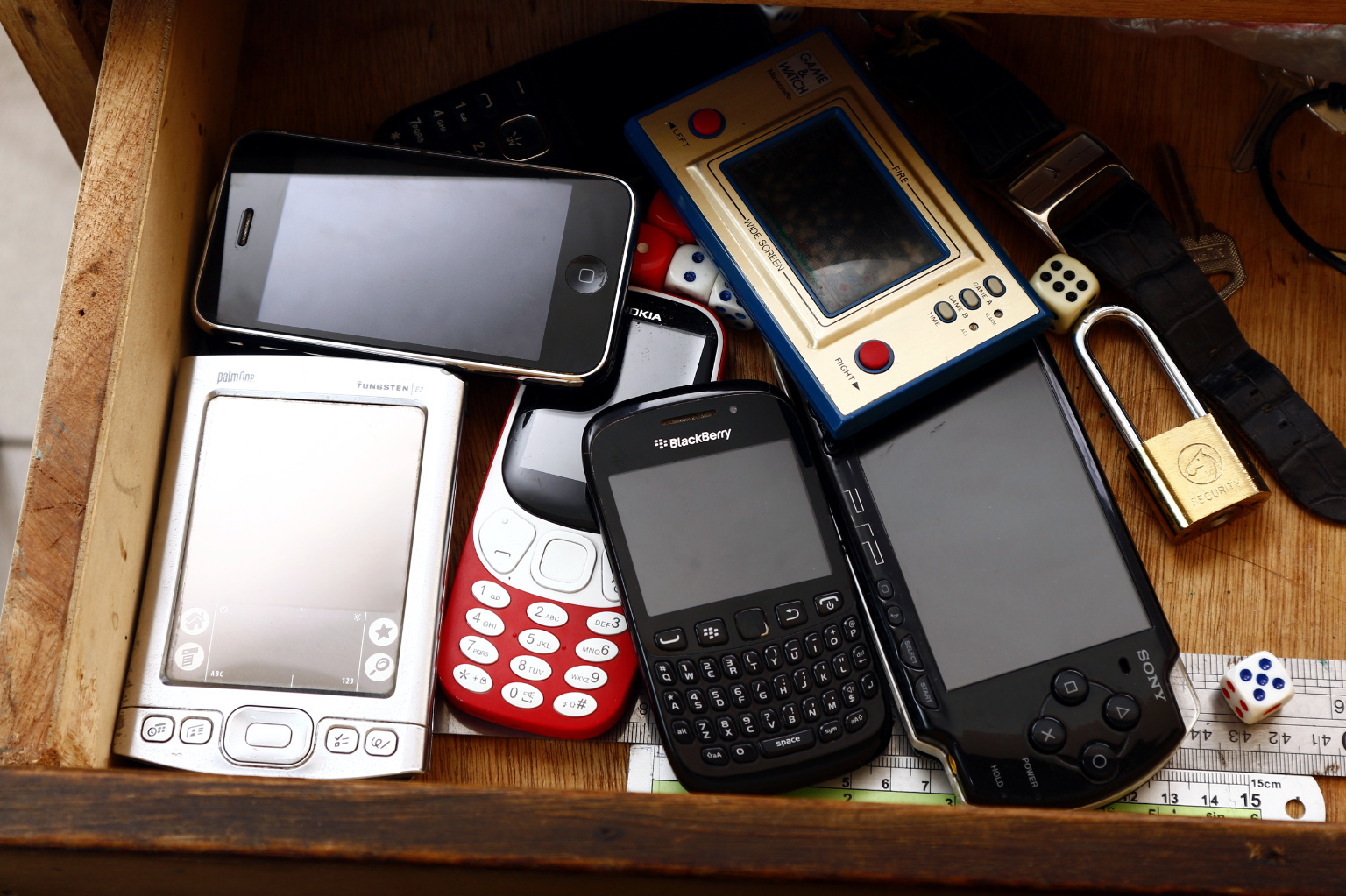 Photo of old and vintage game consoles, qwerty cellphone, smartphone, feature phone and pda or personal digital assistant inside a drawer.