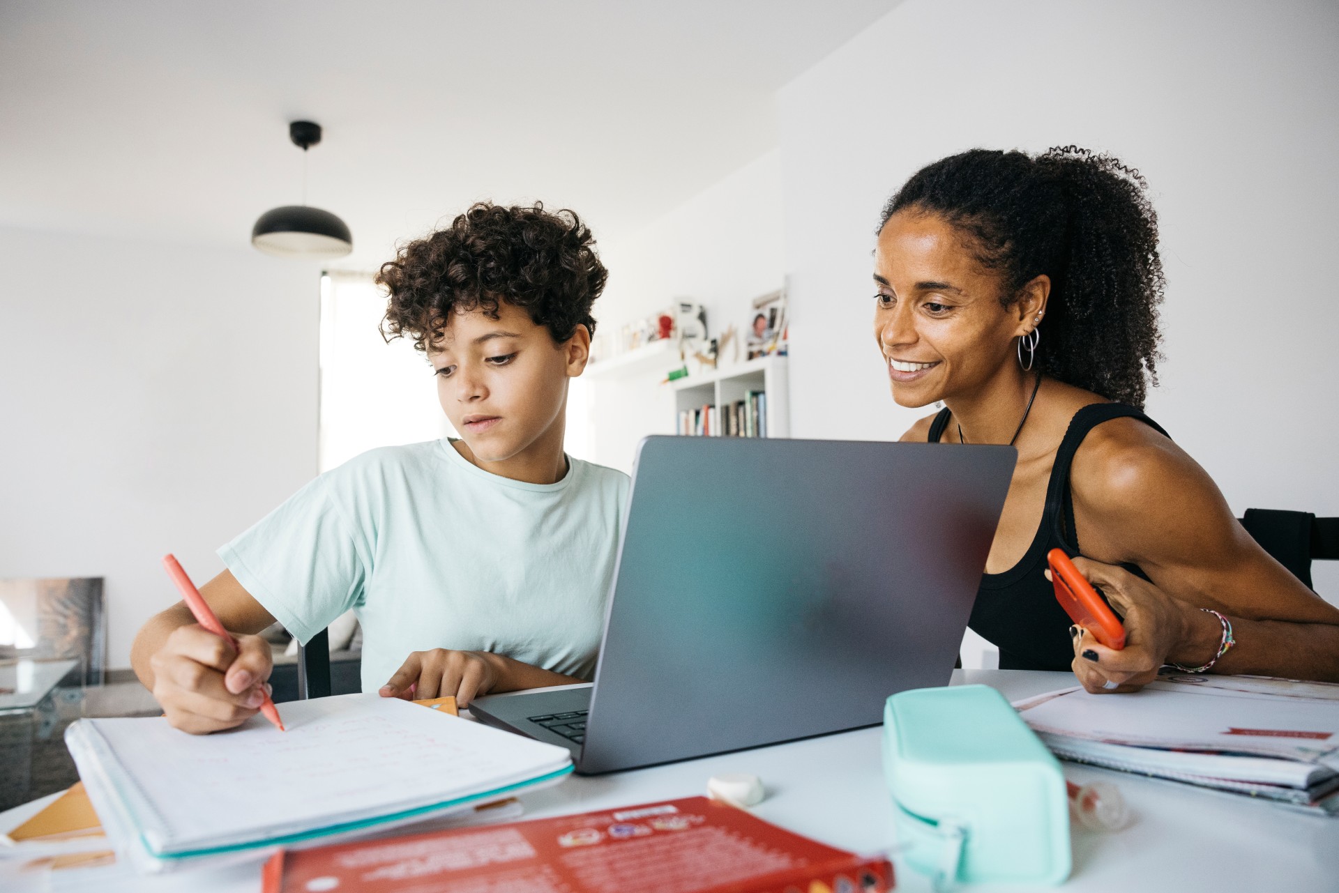 Mother and son at desk with laptop and pad of paper.